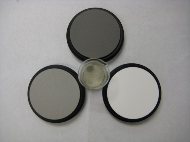 Example of space weathering characterised by darkening and reddening of body surfaces. The material in the middle is a sample of powdered olivine after laser irradiation. The three pads around the sample are light reflectivity standards - the lightest one represents 50%, the darkest one 99% and the third one 80% of reflected light. Photo by M.M.Markley